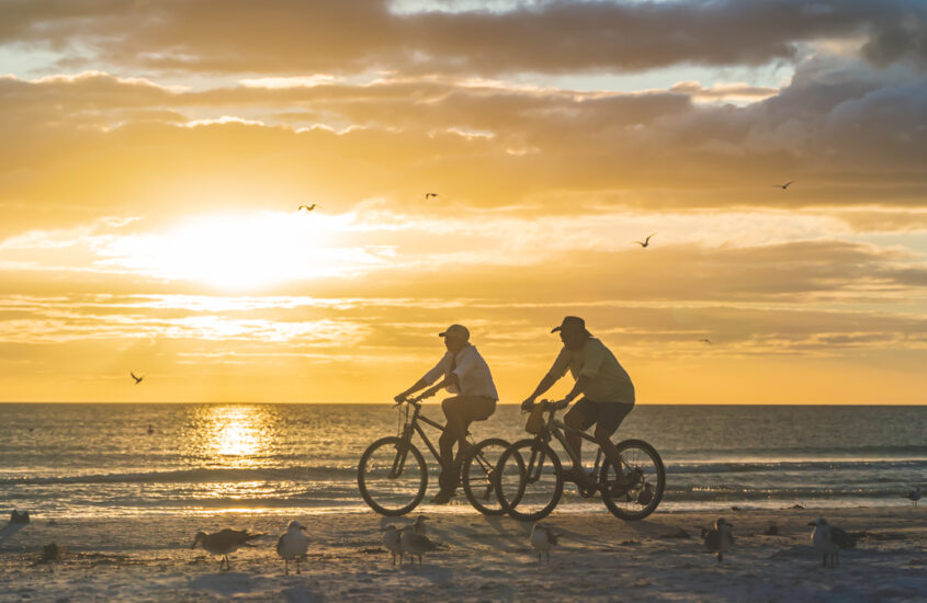 two people ride e bikes on the beach at sunset in silhouette © Joel Hartz