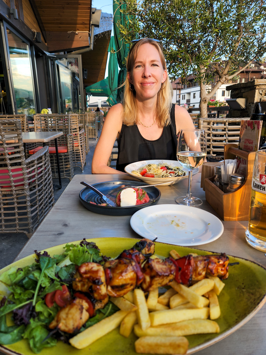 Vertical image of a blonde woman at an outdoor table with food and a glass of wine