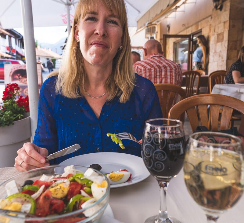 travel blogger michelle hartz enjoying a shopska sald and glass of red wine at outdoor table in bansko bulgaria. wanderinghartz.com