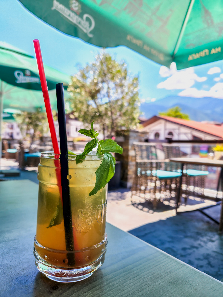 Drink with fresh mint sprig and two straws in foreground and out of focus view of pirin mountains in background