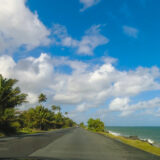 Point of view form car of Puerto Rico roadway along coastline with tropical palm trees, and beautiful sky