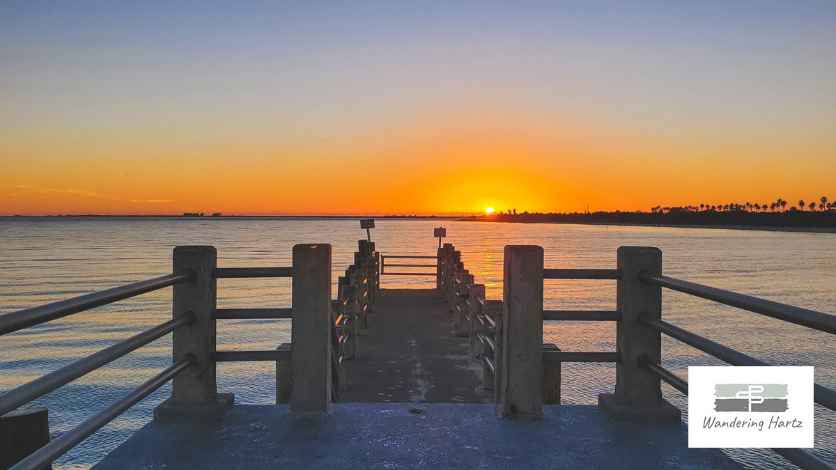 the sun setting over the horizon from the pier at fort de soto park with the palm trees in silhouette