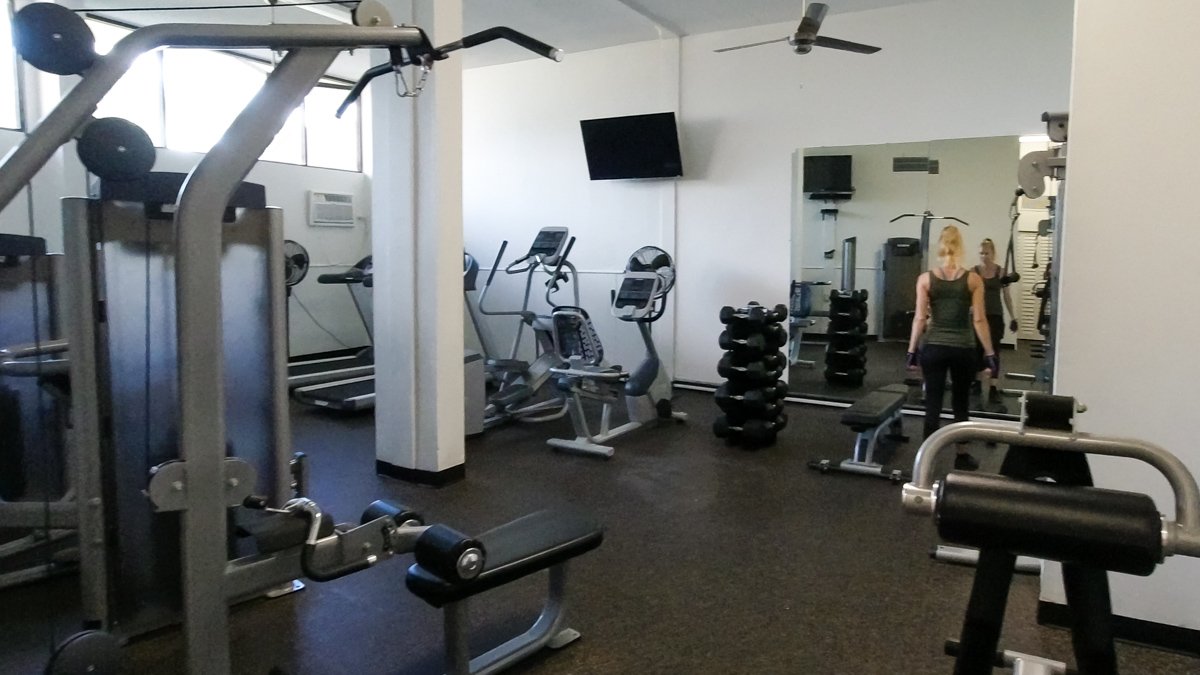 gym full of machines and treadmills with woman in background at mirror © Joel Hartz