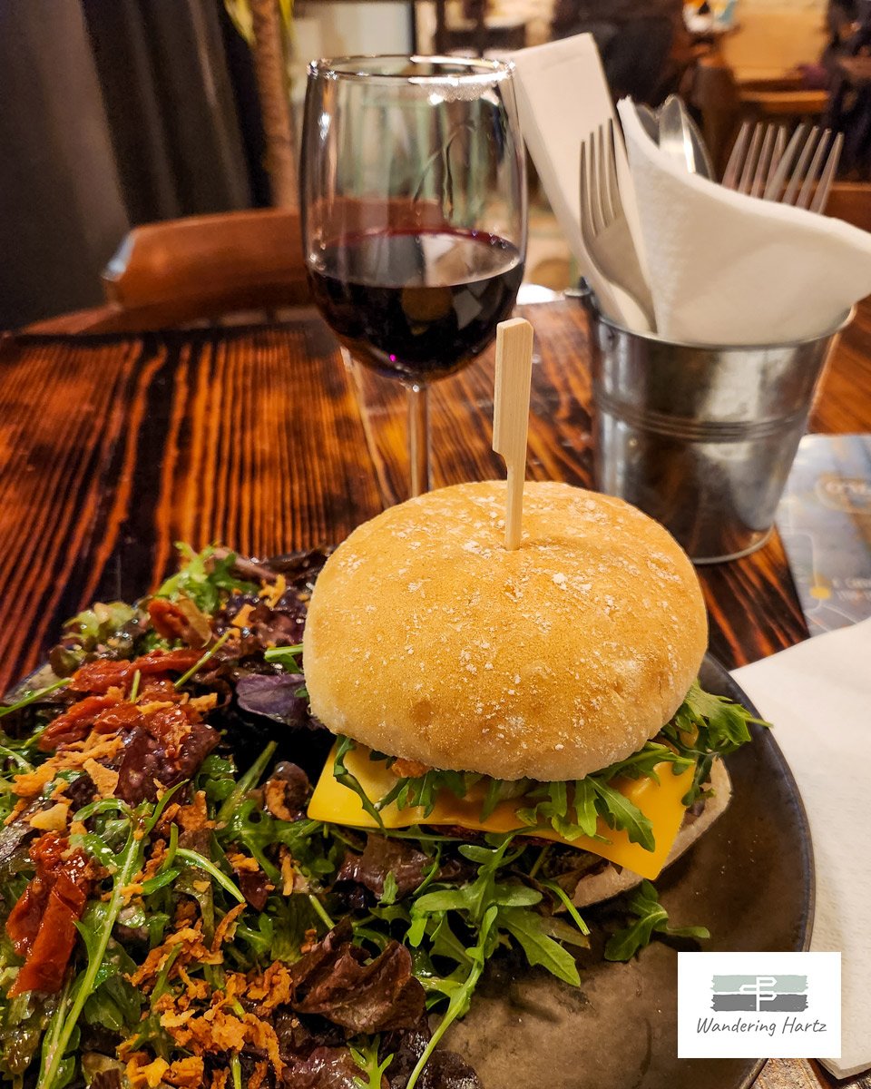 plate with a veggie burger and salad on table with glass of red wine