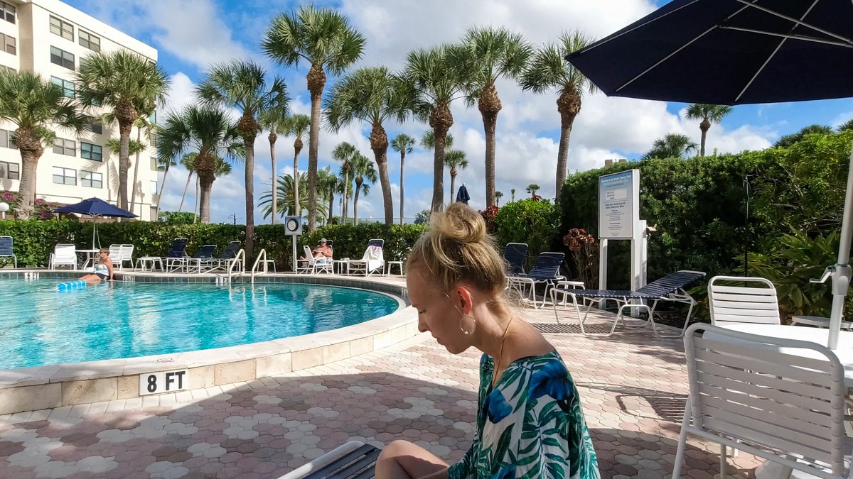 woman sitting at pool with palm trees in background © Joel Hartz