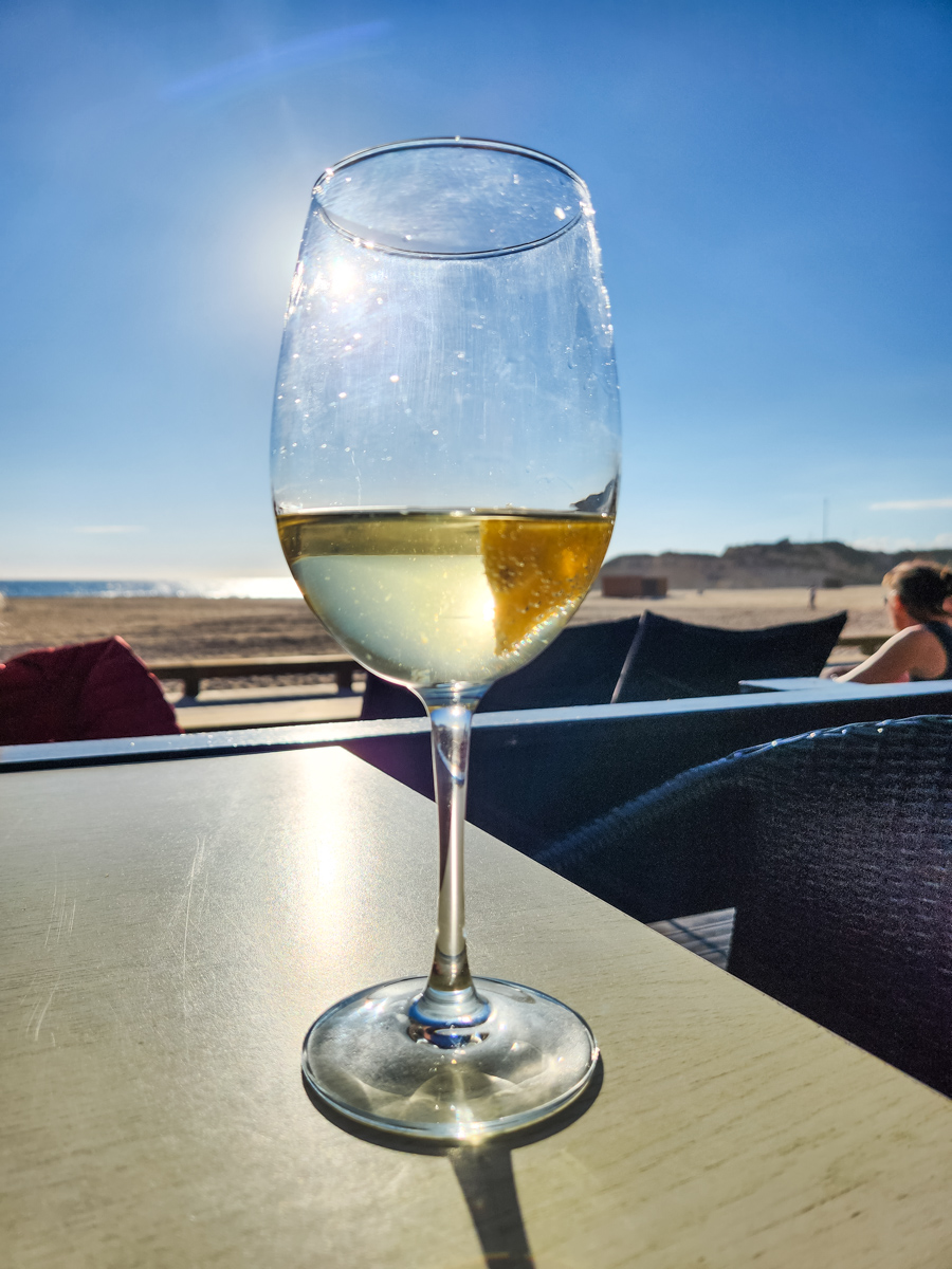 glass of white wine on table backlite by the sun on clear day at the beach