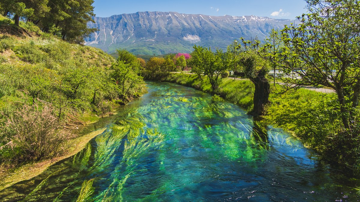 colorful scene of crystal clear river fed by Viroit Spring in Albania with the Drino Mountains in background