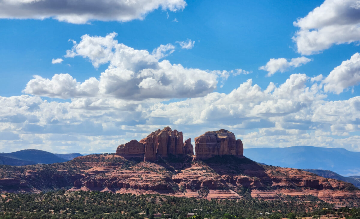 view of cathedral rock in sedona with blue sky and white puffy clouds