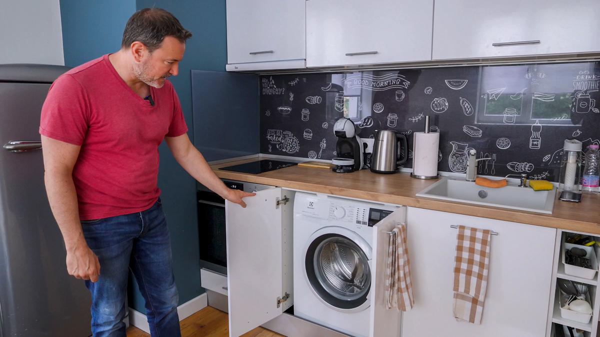 man showing the interior kitchen and washing machine of apartment during tour 