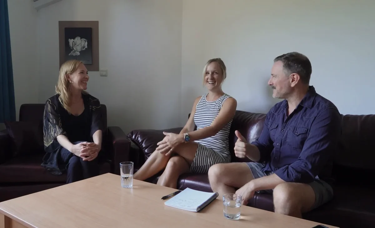 Three people sit on a couch, engaged in a conversation around a coffee table.
